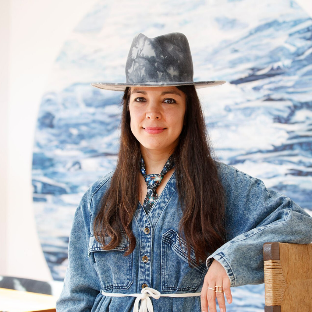 woman with long dark hair and a denim hat smiling