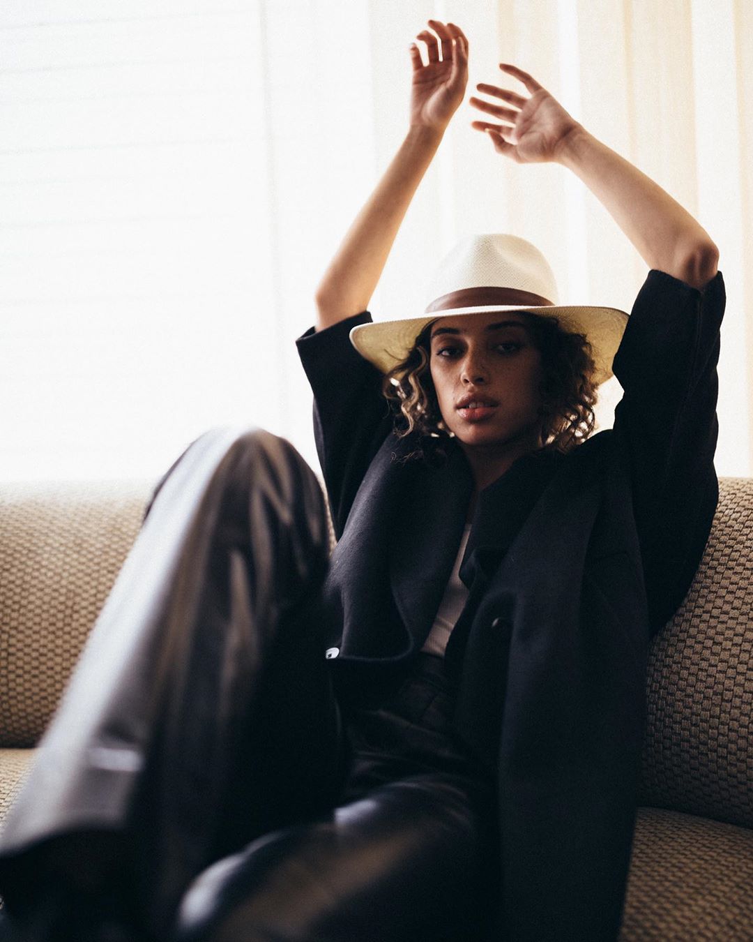 woman in hat sitting on couch with arms in the air