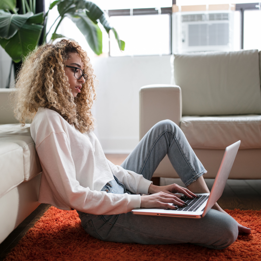 curly haired woman sitting on floor with laptop